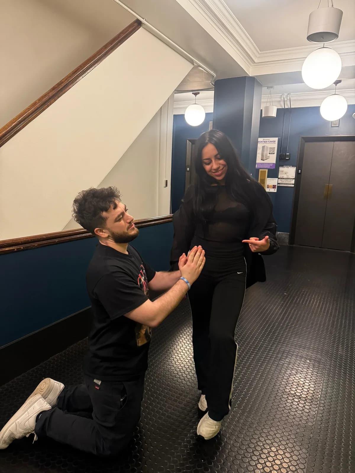 Michalis kneeling in front of Cristal in a dim hallway